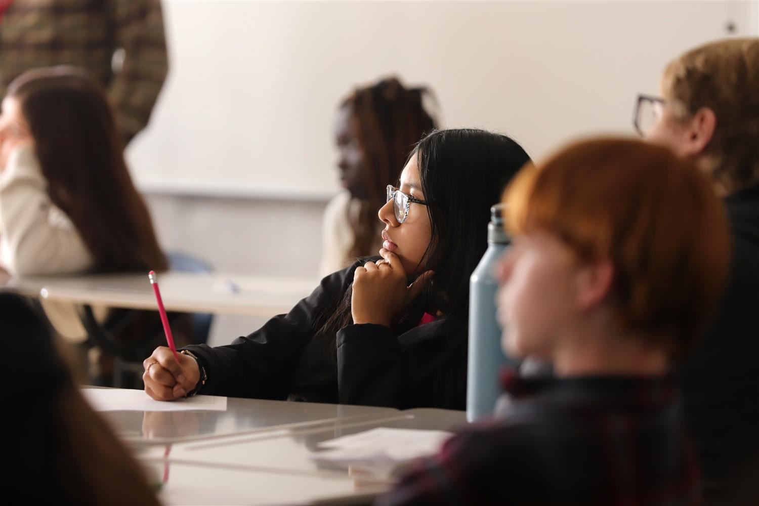  GISH Freshman Student at desk writing with a pencil while listening to teacher in class.